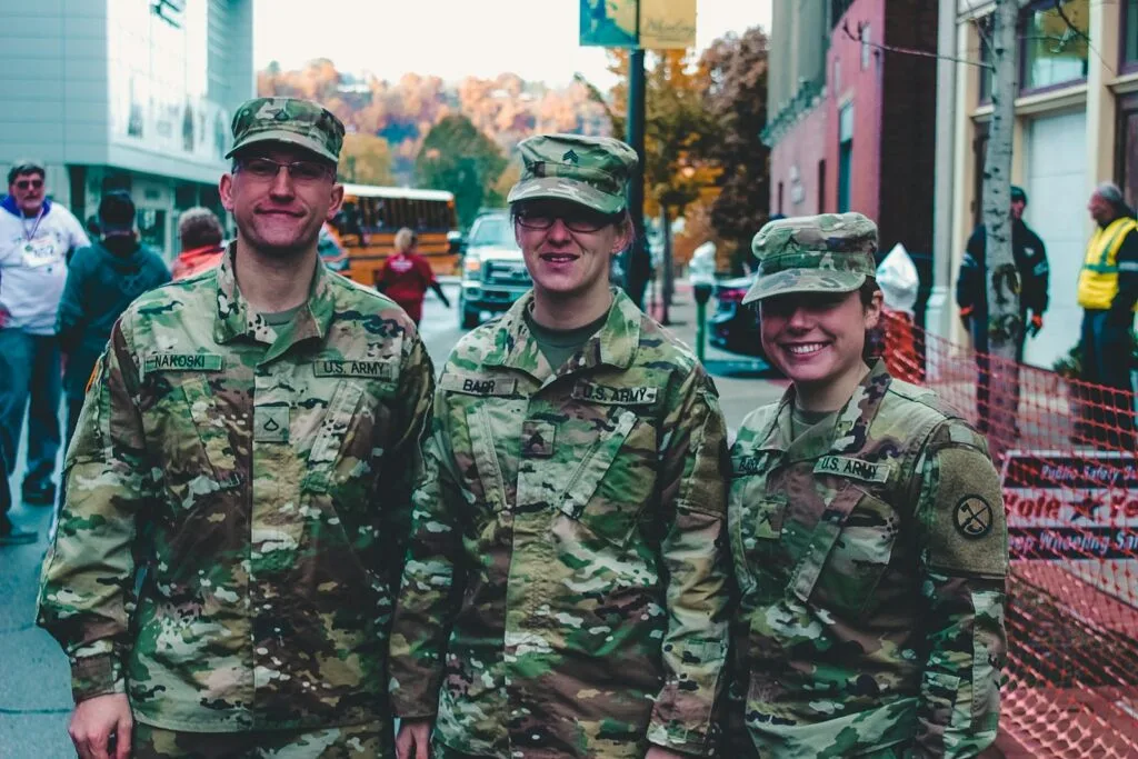 Three US Army soldiers in camouflage uniform smiling at a public event in Wheeling, WV.