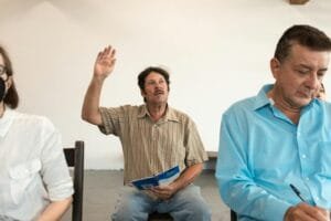 Adults engaged in a classroom setting, raising hands and taking notes.