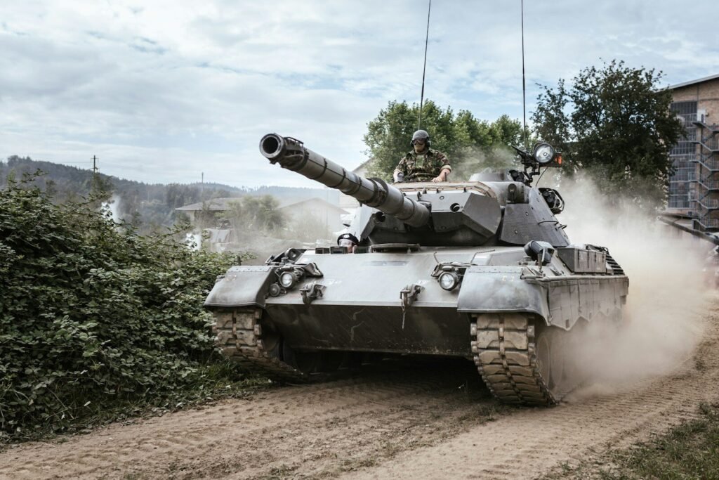 A military tank driving on a dirt road, kicking up dust, with a soldier visible