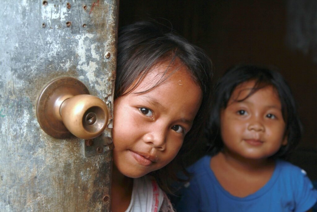 Two curious children peek through a doorway